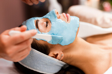 Procedure for skin care. Doctor in cosmetology office applies an alginate mask to the face of young pretty woman.