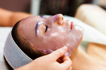 The beautician applies a transparent jelly peer mask to the girl's face. Facial skin care. Pore ​​removal and skin exfoliation. - obrazy, fototapety, plakaty