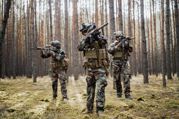 Squad of Four Fully Equipped Soldiers in Camouflage on a Reconnaissance Military Mission, Aiming Rifles. They're Moving in Formation Through Dense Pine Forest.