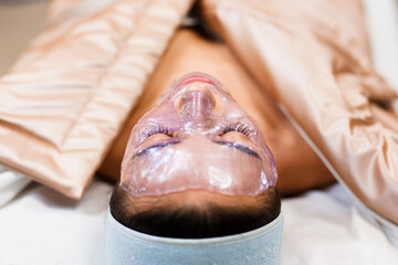 The beautician applies a transparent jelly peer mask to the girl's face. Facial skin care. Pore...