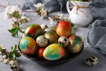 Marble Easter eggs painted with multi-colored food colors and quail eggs in a plate on a gray background. Close-up.