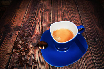A blue coffee cup with cream coffee stands on a dark brown wooden surface.