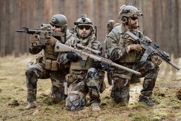 Portrait of a middle-aged bearded soldiers in a Woodland military uniform and helmet, with headphones on his head holding a rifle.