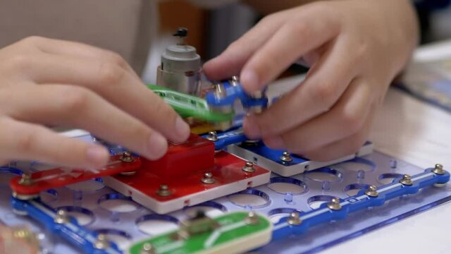 Curious Boy Assembles Electrical Circuit of Metal Construction Kit Parts. Zoom