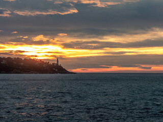 Fototapeta na wymiar Lever de soleil sur la mer et le phare de la presqu'île du Cap Ferrat près de Nice sur la Côte d'Azur