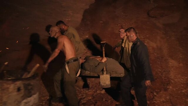 Men in the mine carry their friend on a stretcher. Gold miners are looking for jewelry.