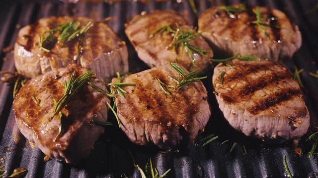 Delicious juicy meat steak cooking on grill. Aged prime rare roast grilling tenderloin fresh marble tenderness beef. Prime beef fry on electric roaster, rosemary, black pepper, salt. Slow motion.