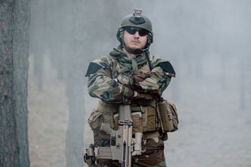 Fully equipped soldier in a camouflage uniform emerging from a puff of smoke in the middle of a...
