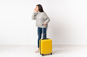 A full length body of a traveler woman with a suitcase over isolated white wall shouting with mouth wide open