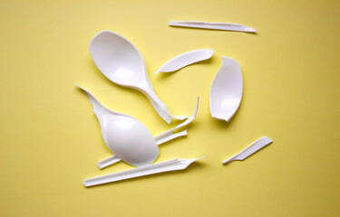 Broken disposable plastic white spoons. Broken plastic on a yellow background. Disposable cutlery.