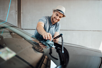 Young handsome man with hat cleaning car with rag, car detailing (or valeting) concept.