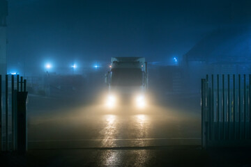 Truck leaving a factory at night on a very foggy day with poor visibility.