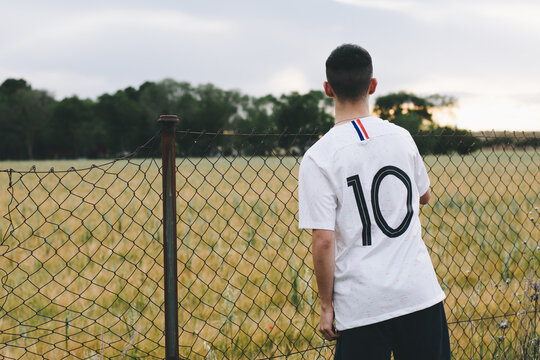 Joven con camiseta de fútbol apoyado en una valla mirando el horizonte