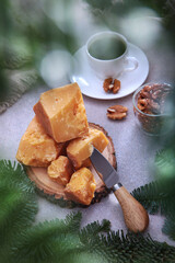 Slices of hard cheese with a cheese knife on a light background. Walnuts and honey. A white cup of coffee. Spruce branches.