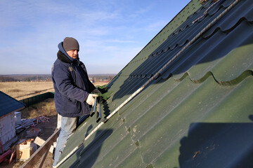 Installation of the roof of the house is done by a worker, snow guards and other roof elements.