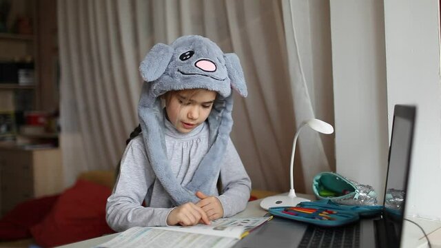 Distant education, online class meeting, reading. Pretty schoolgirl wearing funny rabbit hat with ears to amuse classmates during lesson at home, social distance during quarantine, self-isolation