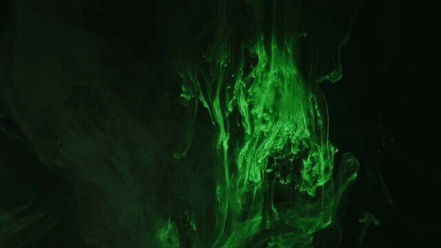 Green paint drops mixing in water slow motion. Smooth ink swirling and splashing from above underwater. Ink cloud on black background. Colored abstract smoke explosion.