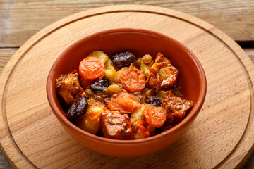 A dish of Jewish cuisine tsimes with carrots, dates and turkey meat in a clay plate on a wooden round stand.