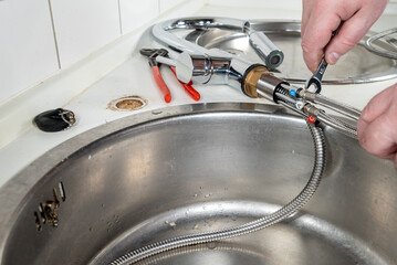 Plumber installing a mixer tab on a sink in the kitchen