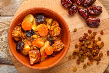 A dish of Jewish cuisine tsimes with carrots, dates and turkey meat in a plate on a wooden background next to raisins and dates sprinkled.