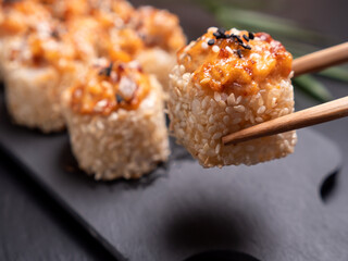 Take one Sushi roll with baked eel from black slate plate. One piece in chopsticks