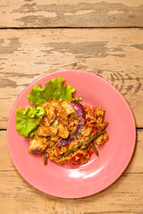 Vegetables with rice and chicken in Pan-Asian sauce and sesame seeds on salad leaves on a wooden table in a plate.