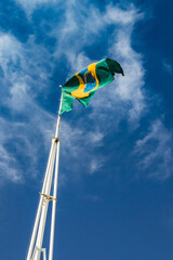 National flag of Brazil on white flagpole and blue sky