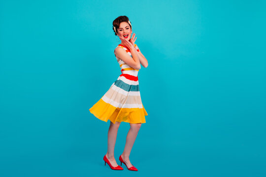 Full length view of pinup girl in striped dress. Studio shot of brunette lady dancing on blue background.