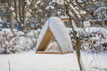 The bird feeder is covered with snow near the school. Wooden bird table topped with fresh snow