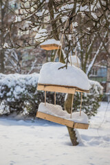 The bird feeder is covered with snow near the school. Wooden bird table topped with fresh snow