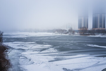 Winter landscape. Frozen river in fog on a cloudy day. Tall buildings in the fog on the river bank. Dnipro. Kyiv, Ukraine