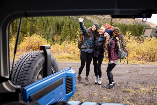 Happy Young Women Friends With Hiking Backpacks Taking Selfie At Jeep