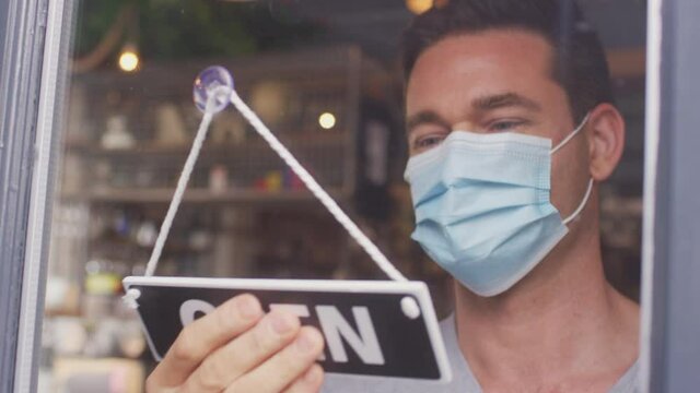 Male owner of small business wearing face mask turning round open sign in door during health pandemic -  shot in slow motion
