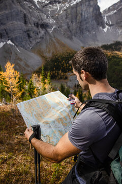 Male backpacker with compass and trail map in autumn mountains