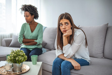 Two upset friends not talking to each other after fight on the sofa in sitting room at home. Two...