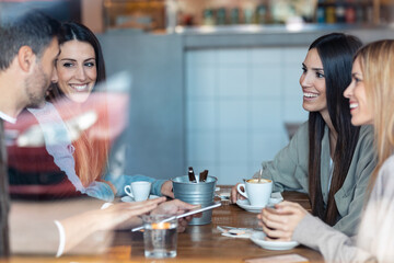 Happy friends group eating burgers while talking about work using digital tablet sitting in restaurant.
