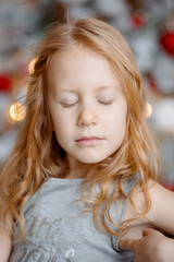 Portrait of a girl with red hair who closed her eyes. Behind her are bright lights and red balloons