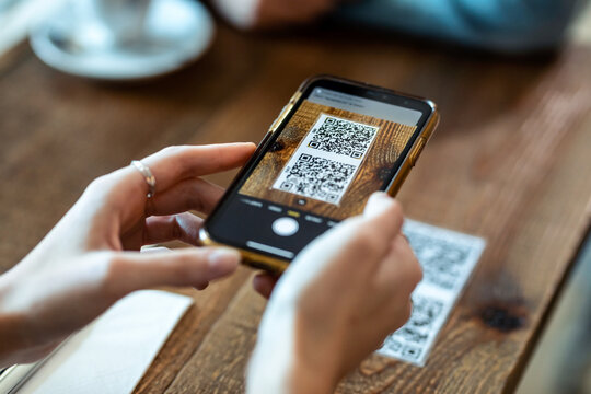Young woman hands using the smart phone to scan the qr code to select food menu in the restaurant.