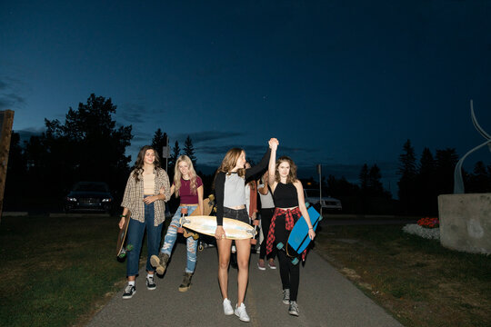 Carefree teenage girl friends with skateboards on path at night