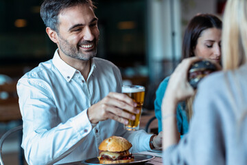 Attractive young friends group eating burgers while talking and having fun in the restaurant.