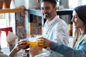 Happy young friends group toasting with beer to celebrating good news while having fun in a restaurant.