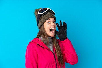 Teenager skier girl with snowboarding glasses over isolated blue background shouting with mouth wide open