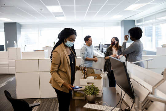 New Hire Businesswoman In Face Mask Unpacking Box In Office Cubicle