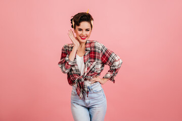 Shapely smiling pinup girl posing on pink background. Front view of playful european lady in checkered shirt.