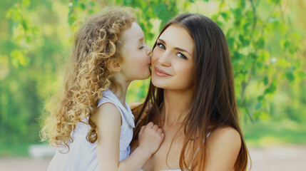 Fototapeta premium Portrait of happy child daughter kissing her mom in a summer park