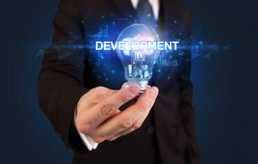 Businessman holding light bulb with DEVELOPMENT inscription, innovative technology concept