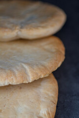Pita Brot drei Stück leicht gebräunt hintereinander aufgelegt mit dunklem Hintergrund, niemand