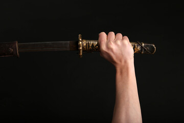 A handle of a sword in a hand on black background