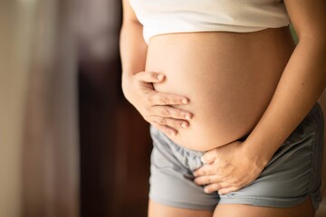 Pregnant woman holding her belly needing to pee with a week bladder. Constipation and bladder...