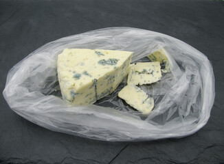 Triangular sliced piece of cheese with blue Dorblu mold in a transparent bag.